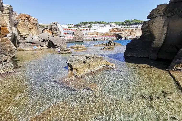Le vasche di roccia del Bagno Marino Archi, con l'acqua bassa e trasparente e il paese sullo sfondo.