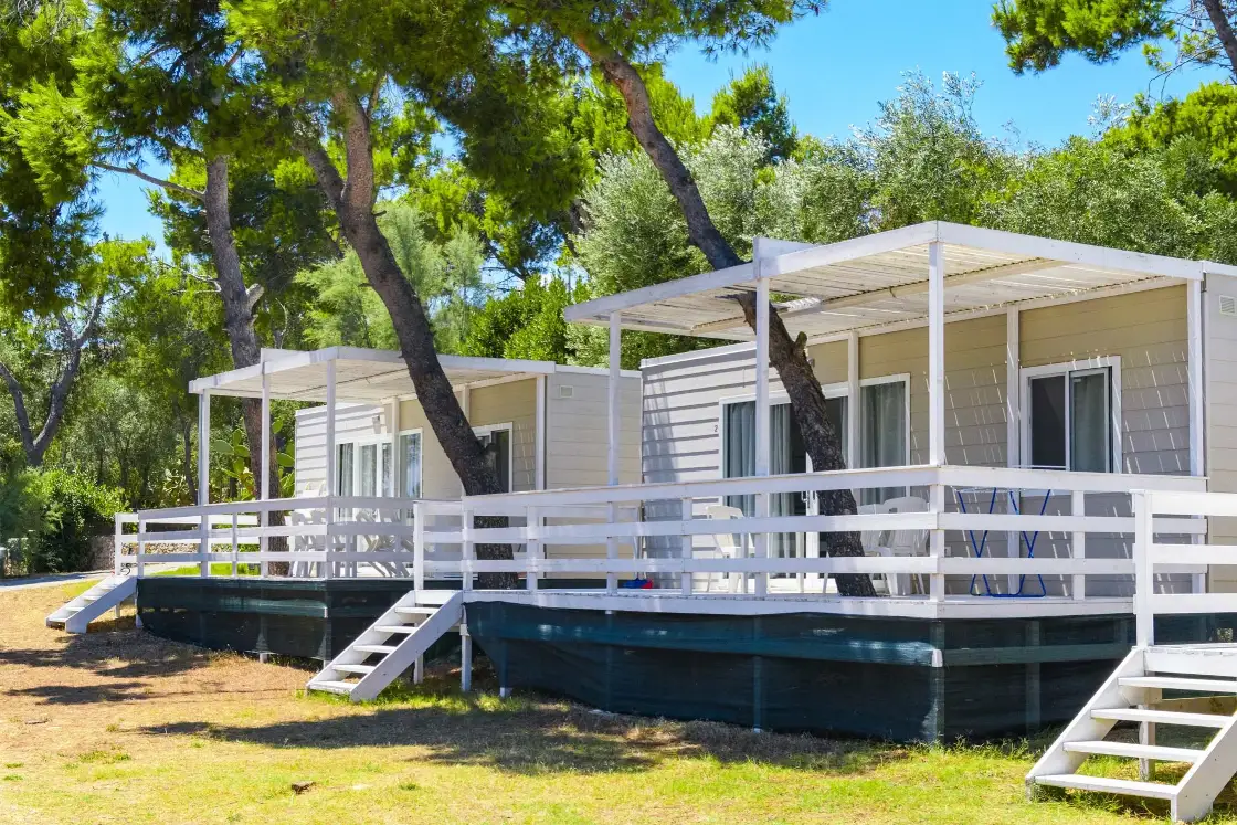 Mobile Home Deluxe con la veranda bianca e le scalette, tra i pini