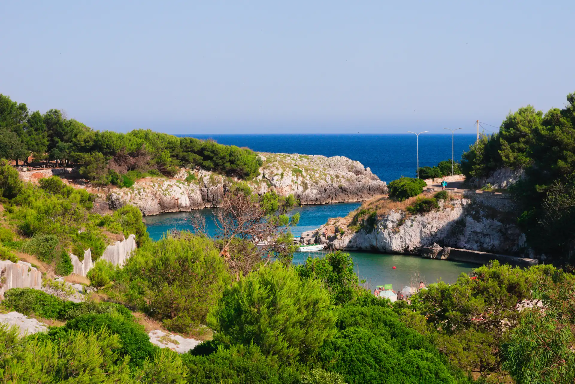 Un'insenatura di acqua turchese fra la macchia mediterranea, con il mare aperto all'orizzonte