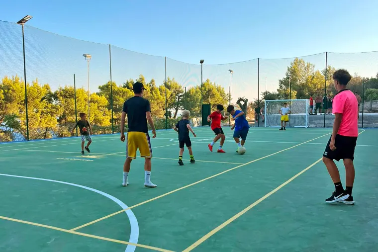 Partita di calcetto sul campo sportivo, tra la rete e i pini