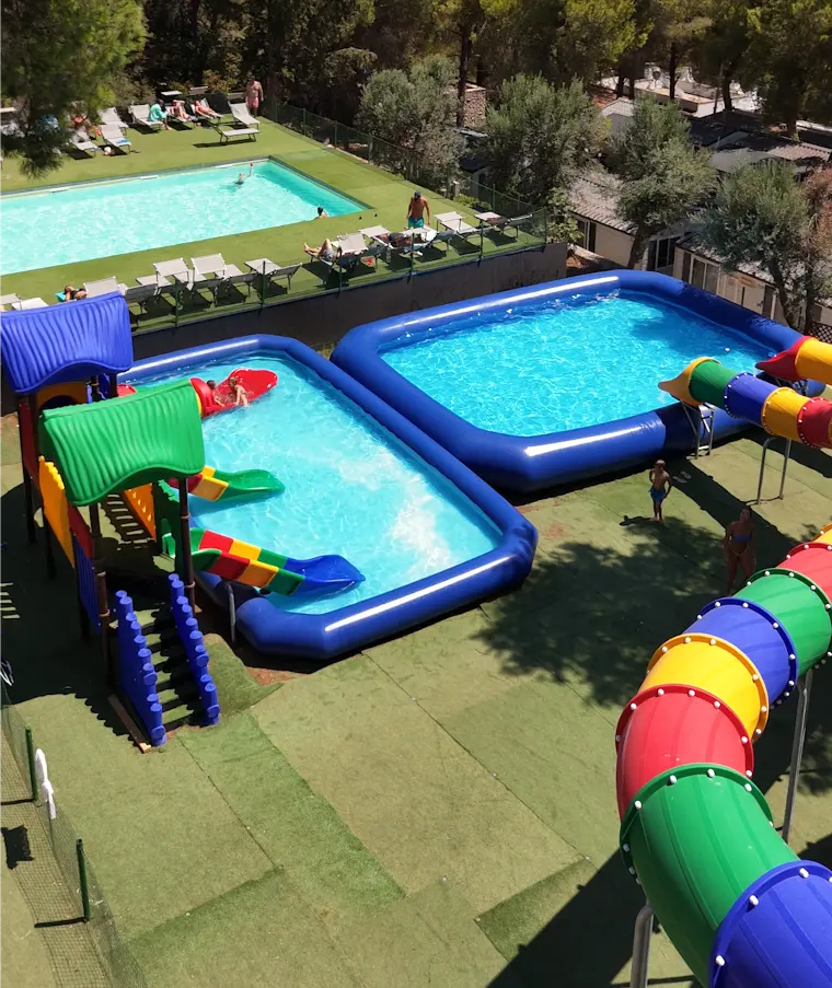 Le piscine con gli scivoli viste dall'alto, tra il prato e la pineta