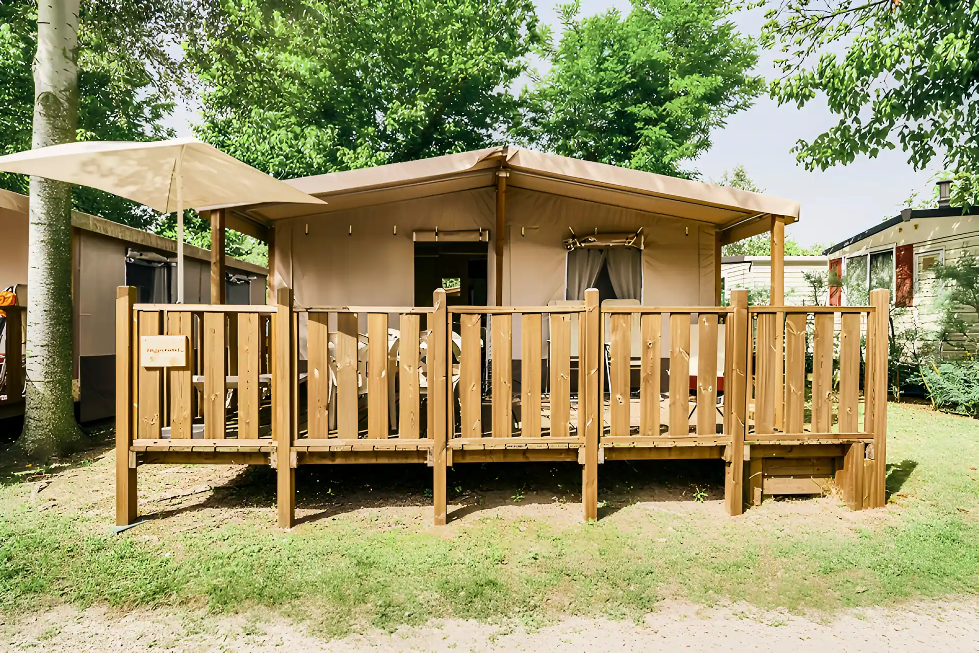 Tenda lodge con veranda in legno tra gli alberi del camping